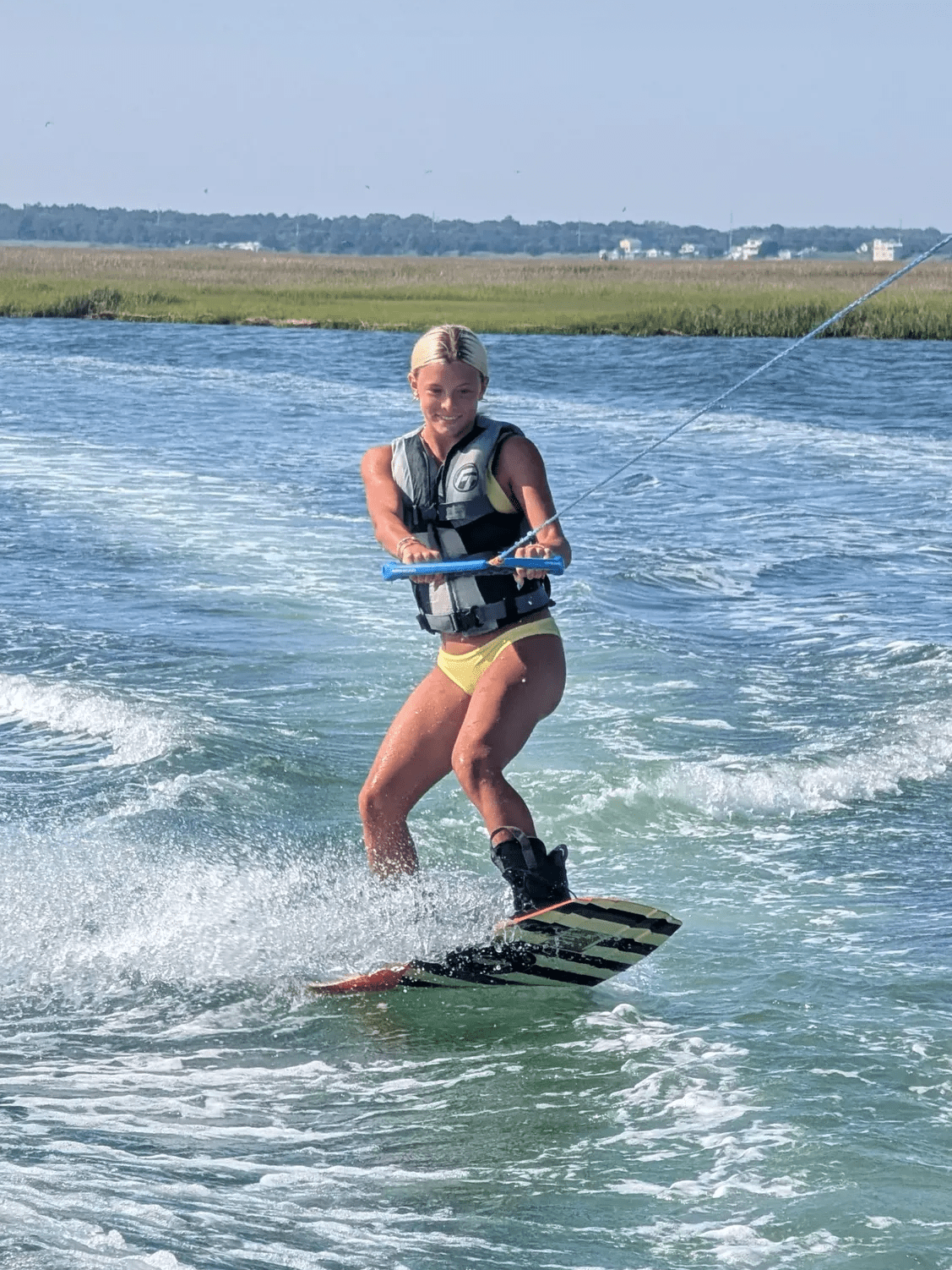 Teen wakeboarder riding across the Stone Harbor back bay with the spartina marsh and houses visible across the water.