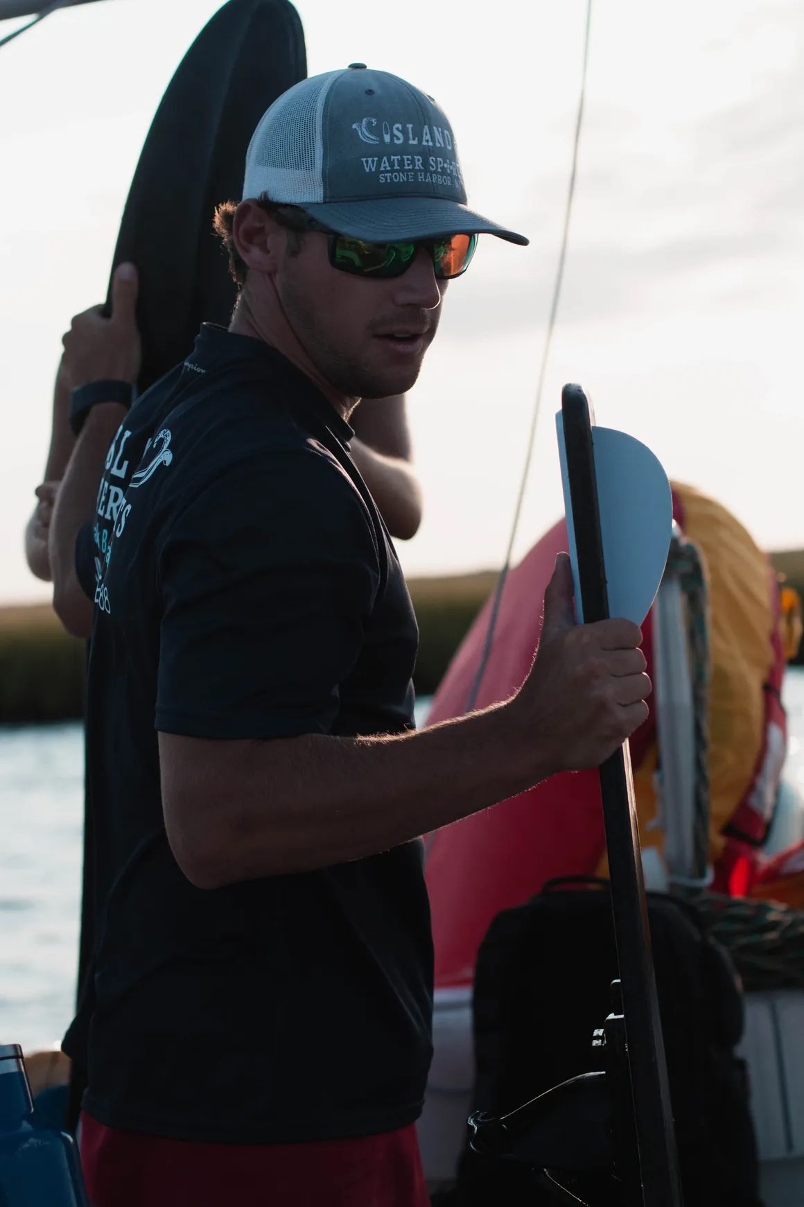 Island Water Sports captain in branded hat carrying gear at golden hour, ready for a back bay water sports session.