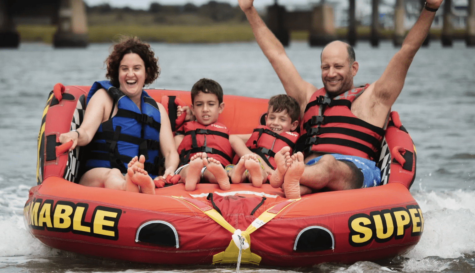 Family of four laughing on a tube, dad with arms raised in celebration
