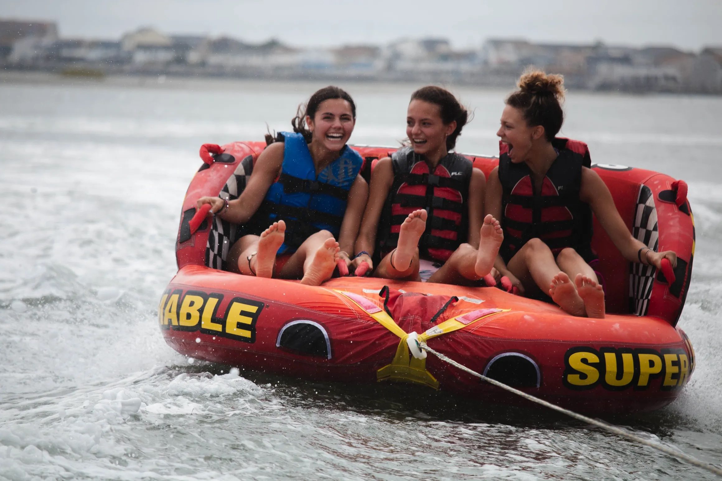 Three teenage friends laughing together on a tube on the back bay