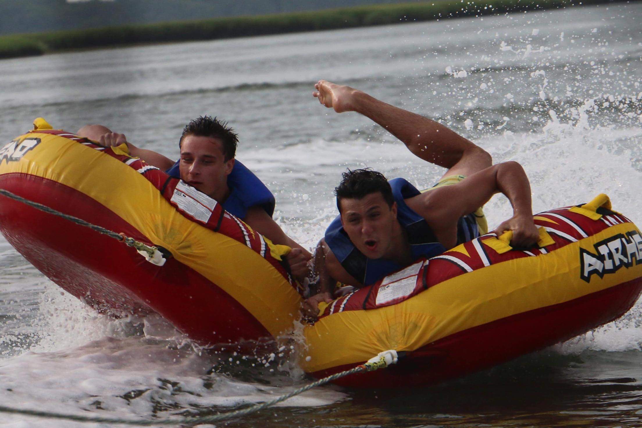 Two guests catching air on a tube behind an Island Water Sports ski boat on the Stone Harbor back bay.