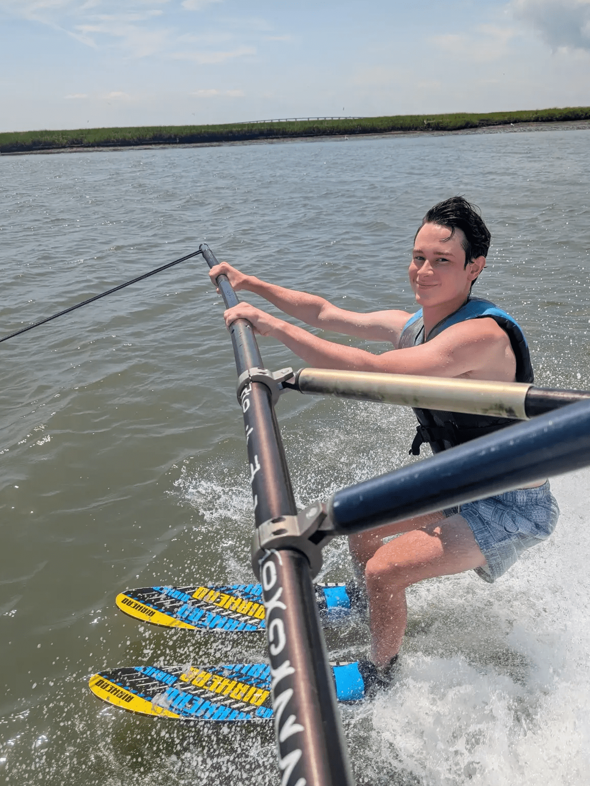Teenage boy water skiing on the boom in the Stone Harbor back bay with marsh in the background.