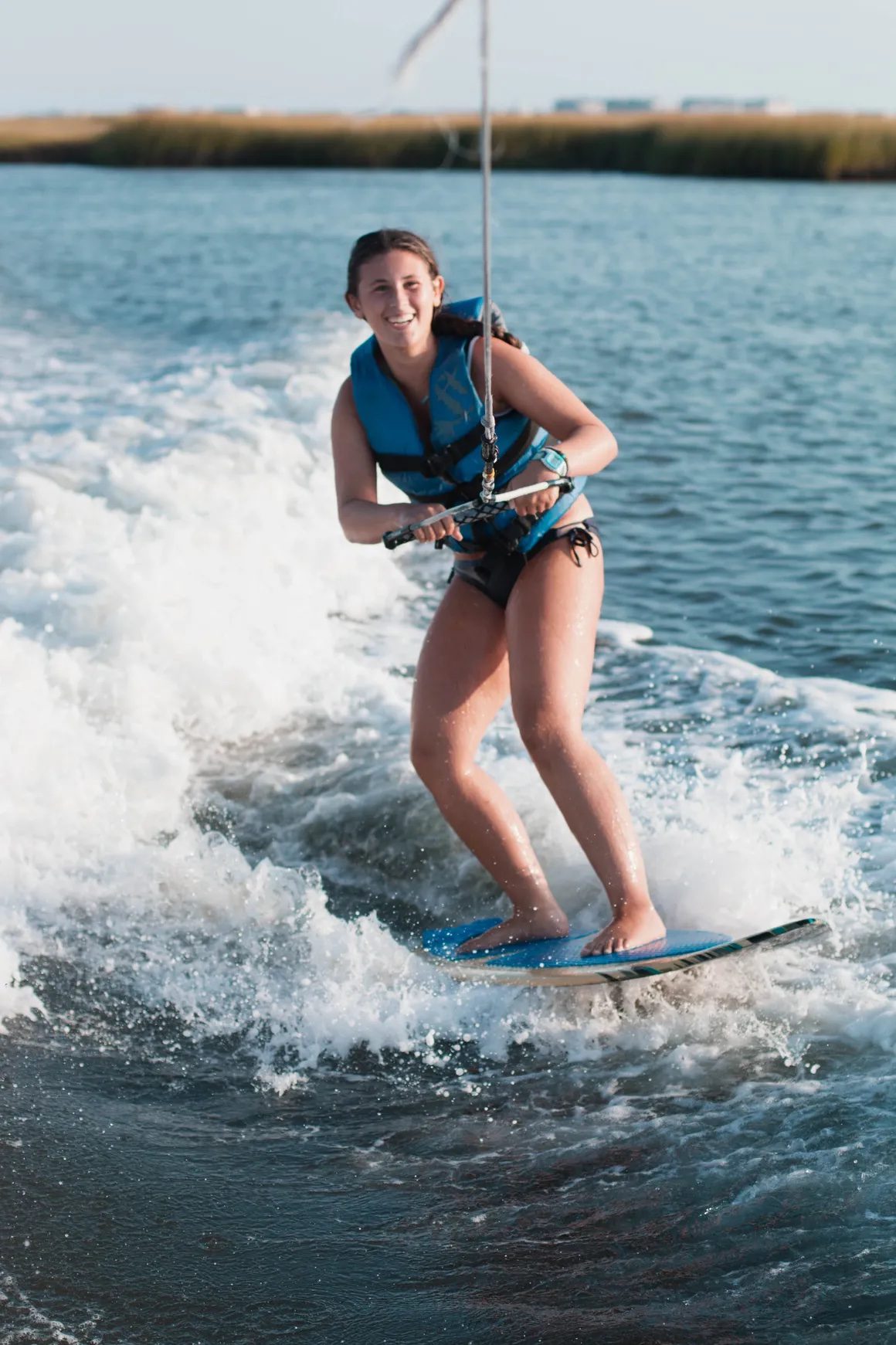 Wakesurfer riding the wave at golden hour with the Stone Harbor back bay marsh behind her.