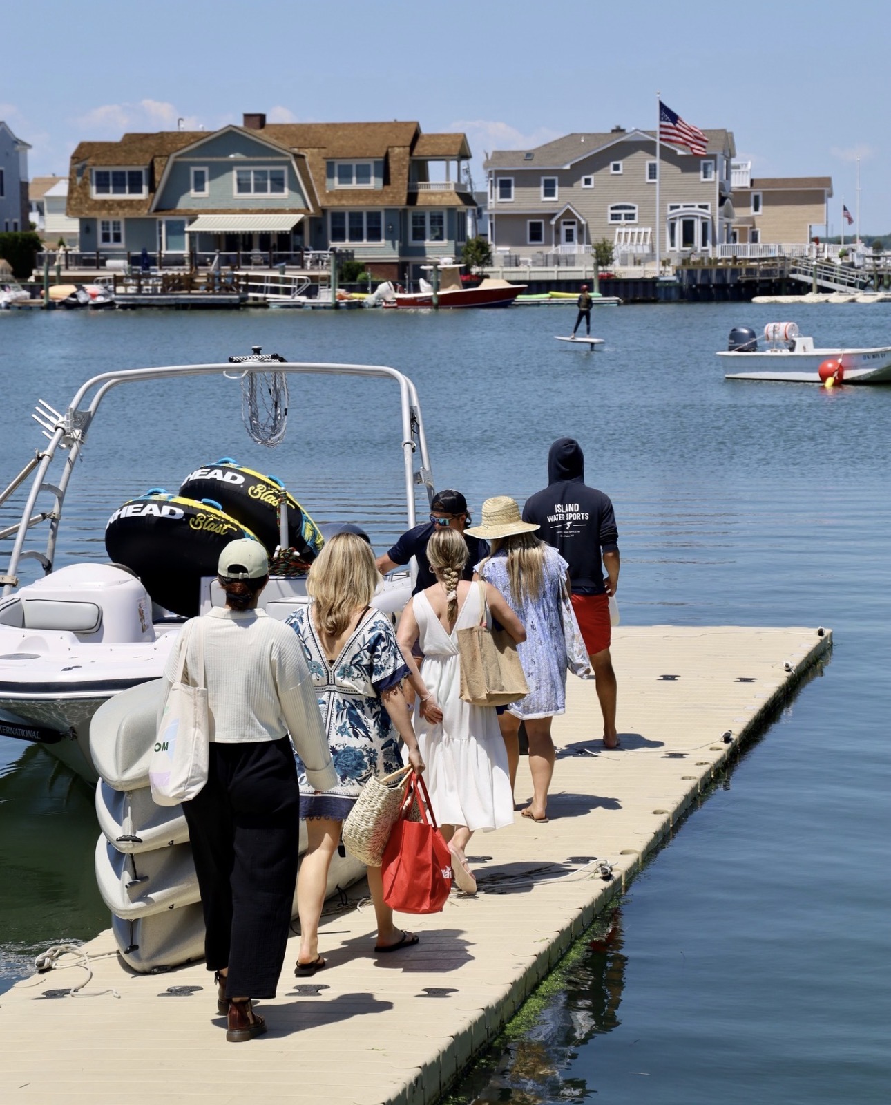Group walking down the Island Water Sports dock toward the ski boat with tubes loaded, Stone Harbor back bay homes in the background.