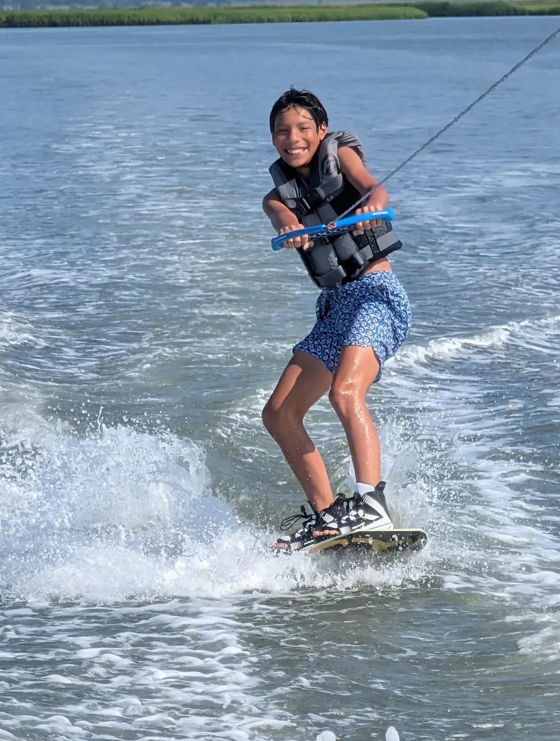 Young rider wakeboarding behind an Island Water Sports ski boat in the Stone Harbor back bay, grinning mid-ride.