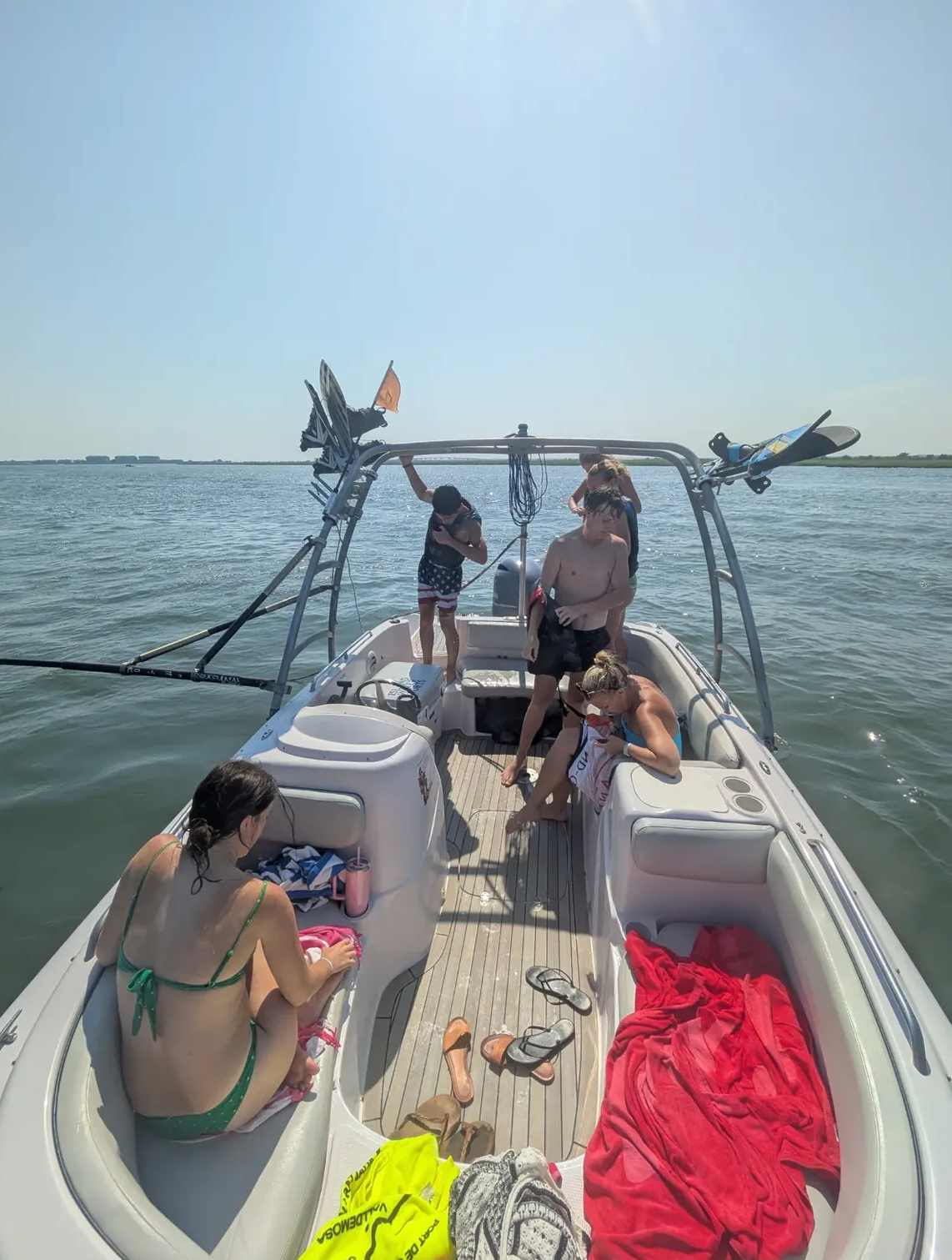 Group relaxing on the Island Water Sports ski boat between activities — wakeboards loaded on the tower, towels and drinks aboard.